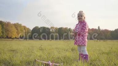 穿着点缀的粉红色夹克和橡胶靴的金发白种人小女孩在户外玩玩具飞机。 可爱